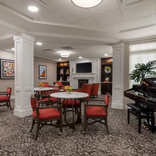 A cozy lounge area with red chairs, round tables, a piano, and a television.