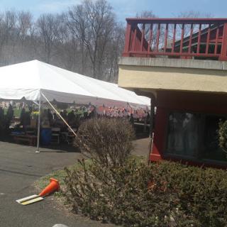 A spacious outdoor tent set up next to a building, surrounded by greenery on a sunny day.