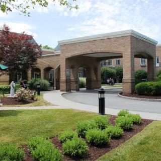 A welcoming entrance to a well-maintained building, surrounded by lush gardens and a clear blue sky.