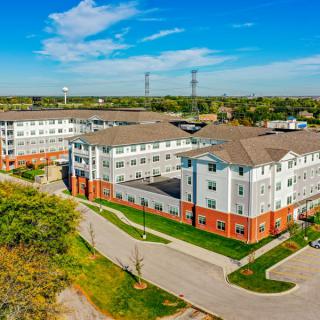 Aerial view of a residential apartment complex with surrounding greenery and a parking area.