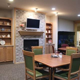 A cozy living room and dining area featuring a fireplace, television, and wooden furnishings with decorative shelves.