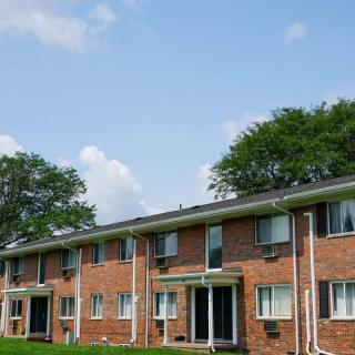A brick apartment building under a clear blue sky with scattered clouds.