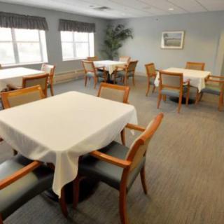 A neatly arranged dining room with several tables and chairs, covered with white tablecloths, and large windows providing natural light.