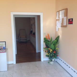 A hallway with a doorway, decorated with a potted plant and a notice board on the wall.