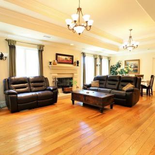 A spacious living room with elegant furnishings, featuring leather sofas, a central coffee table, a fireplace, and stylish chandeliers.