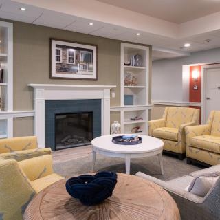 A cozy living room with a fireplace, featuring yellow armchairs and coffee tables surrounded by built-in shelves.