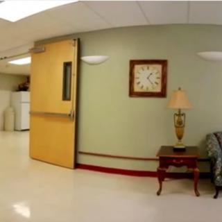 A hospital hallway featuring a clock, lamp, and furniture.