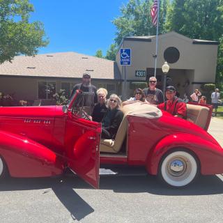 A group of people posing next to a vintage red convertible on a sunny day.