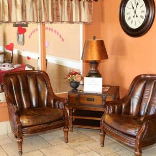 A cozy lounge area featuring two leather chairs, a wooden table with a lamp, and a wall clock.