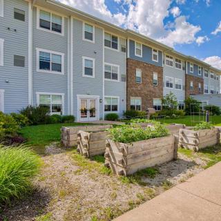 A modern residential apartment building with a landscaped garden and wooden planters under a sunny sky.