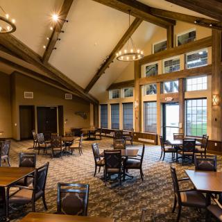 A spacious dining room with high ceilings, featuring tables and chairs arranged neatly under chandeliers and large windows.