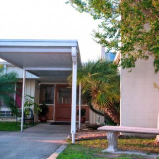 A suburban house with a carport and front entrance, surrounded by trees and a small bench.