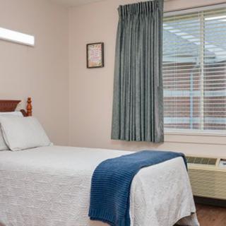 A simple and tidy bedroom with a single bed, featuring a blue throw blanket and curtains.