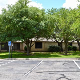 A building with trees in front and an adjacent parking lot featuring a handicap parking sign.