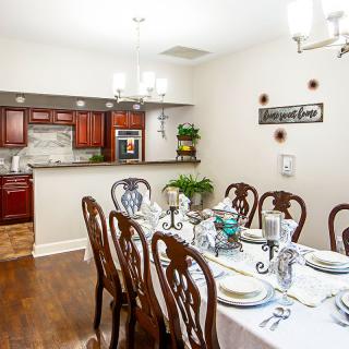 A well-lit dining area featuring a table set for six, adjoining an open kitchen with wooden cabinetry.