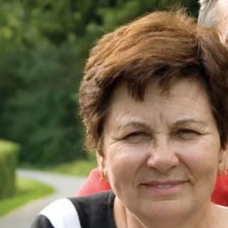 A woman standing outdoors with greenery in the background.