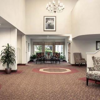 A spacious lobby with elegant decor, featuring a chandelier, carpeted floors, and a comfortable seating area.