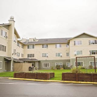 A residential apartment building with three stories, surrounded by a neatly manicured lawn under an overcast sky.
