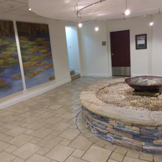 A serene interior lobby featuring a circular water fountain and artistic wall murals.