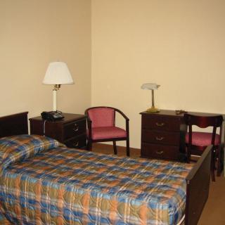 A simple bedroom with a bed, desk, chairs, and lamps.
