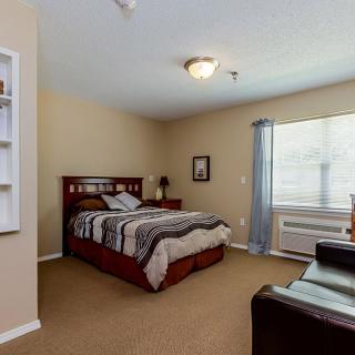 A cozy bedroom with a neatly made bed, soft lighting, and a large window.