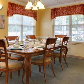A well-appointed dining room featuring a wooden table set for a meal, surrounded by chairs and illuminated by a chandelier, with natural light streaming through the windows.