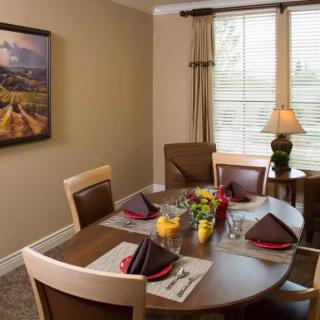 A cozy dining room with a round table set for a meal, featuring neatly arranged place settings and a decorative lamp by the window.