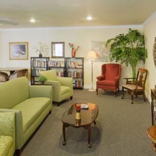A cozy living room featuring a green sofa, armchair, coffee table, and bookshelf with decorative elements.
