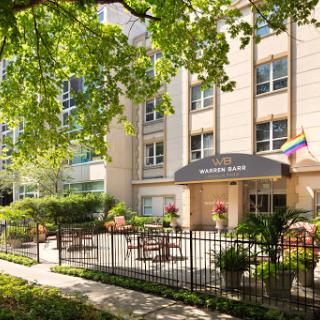 A welcoming hotel entrance featuring a rainbow flag, surrounded by greenery.