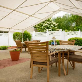 A cozy outdoor dining area set up under a large tent, perfect for gatherings and enjoying the garden view.