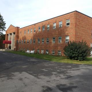 A brick building with multiple windows and a landscaped area, set in a campus-like environment.