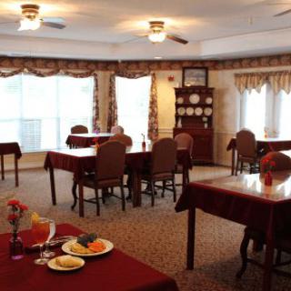 A cozy dining room with several tables and chairs, featuring large windows with curtains.