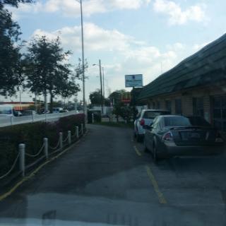 A view of a restaurant's parking lot with cars and trees under a blue sky.