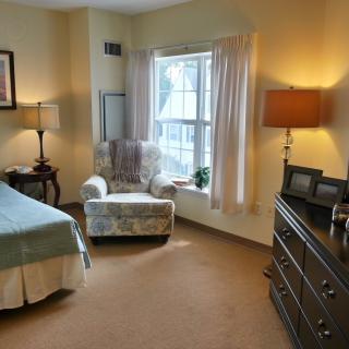 A cozy bedroom with an armchair by the window, a bed, and warm lighting.