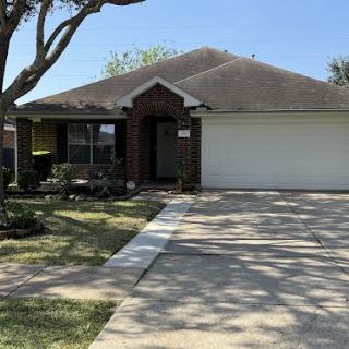 A charming single-story house with a well-maintained front yard and driveway under a clear blue sky.