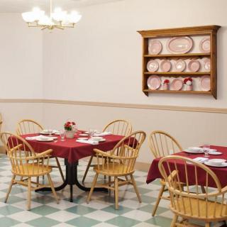 A cozy dining area with circular tables covered in red tablecloths, surrounded by wooden chairs and adorned with a chandelier overhead.