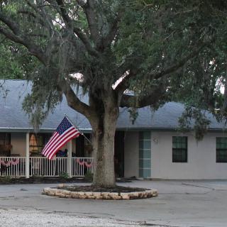 A cozy house with an American flag displayed on the front patio and a large tree in the yard.