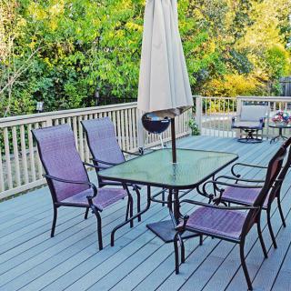A cozy outdoor deck with patio furniture, including a glass table, chairs, and an umbrella surrounded by lush greenery.