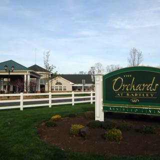 A scenic view of a building with a sign reading 'The Orchards' and a white fence.