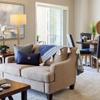 A modern and cozy living room with a sofa, side table lamp, and a dining area in the background.