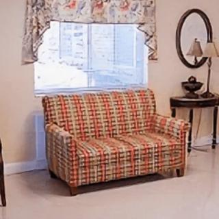 A cozy living room with a plaid-patterned sofa in front of a window, accompanied by a lamp and a side table.