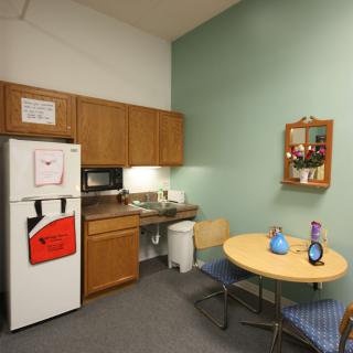 A small break room with a kitchenette, featuring a refrigerator, microwave, and a round table with chairs.