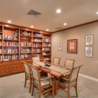 A cozy library room featuring a large wooden table surrounded by chairs, with bookshelves lining the walls.