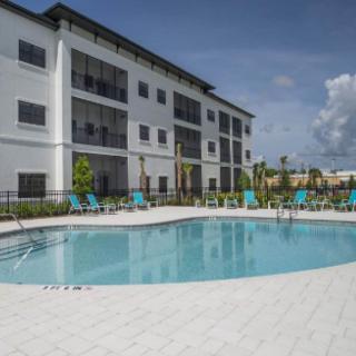 A modern apartment complex with a swimming pool under a clear blue sky.