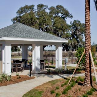 A gazebo with outdoor seating set in a landscaped park area featuring palm trees and pathways.