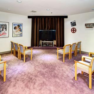 A small theater room with rows of chairs facing a television, decorated with movie posters and curtains.