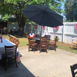 A backyard patio setup with tables, chairs, and a large umbrella for shade.