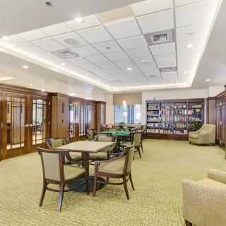 A well-lit room with tables and chairs, featuring a wall of bookshelves.