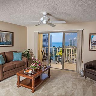 A cozy living room with a balcony view of the ocean, featuring comfortable seating, a coffee table, and decorative elements.