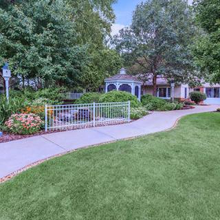 A beautifully landscaped garden with a winding pathway leading to a quaint building surrounded by trees and flowers.